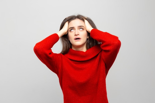 Young woman in a red sweater with a severe headache holds her head isolated on a whitegray background