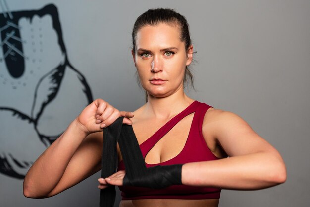 A young woman in a red tracksuit wraps her hands with boxing bandages