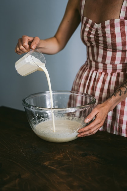 young woman in a red and white checked dress baking a cake, pouring heavy cream to a big glass