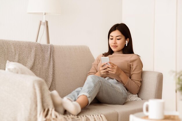 Photo a young woman relaxes on a beige couch legs extended and looks at her phone