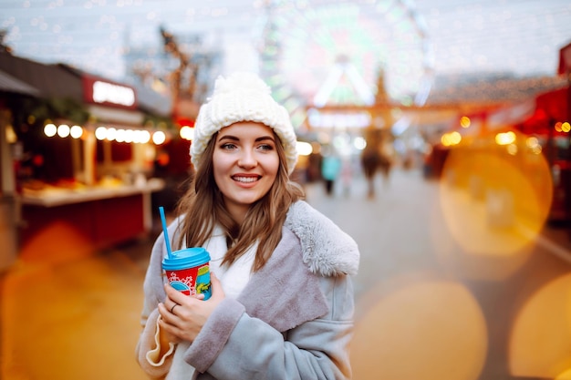 Young woman relaxing drinking coffee in Festive Christmas fair Winter holidays Lights around