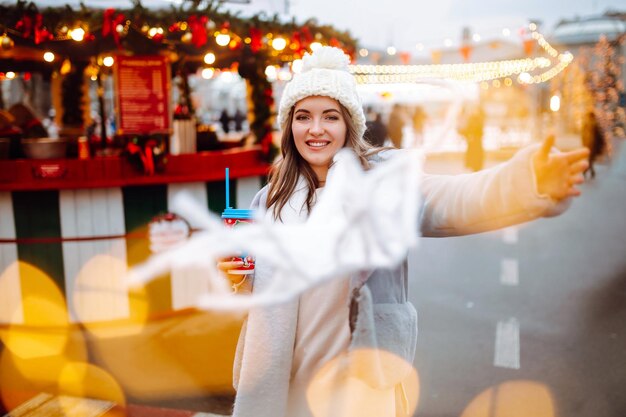 Young woman relaxing drinking coffee in Festive Christmas fair Winter holidays Lights around