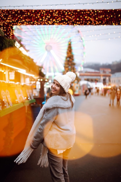 Young woman relaxing drinking coffee in Festive Christmas fair Winter holidays Lights around