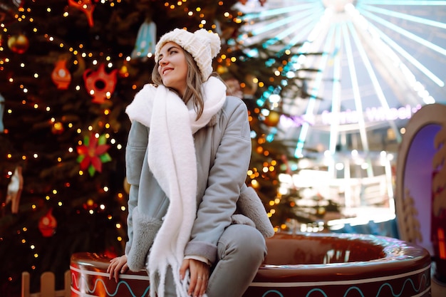 Young woman relaxing drinking coffee in Festive Christmas fair Winter holidays Lights around