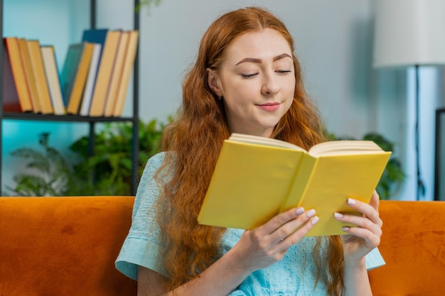 Young woman relaxing interesting book turning pages smiling enjoying literature taking rest on sofa