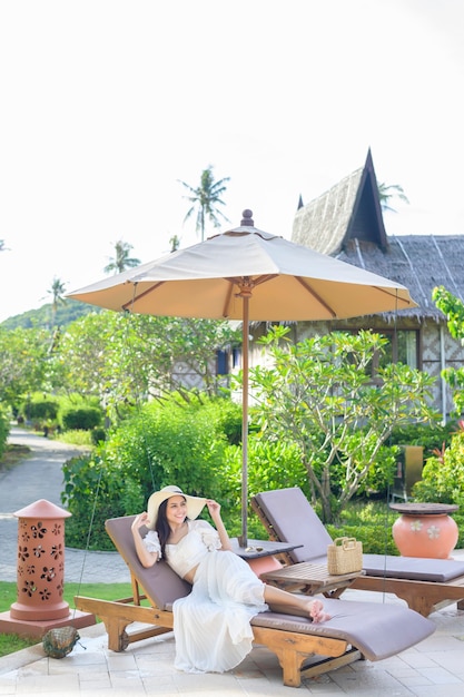 A young woman relaxing and sitting on the lounge chair looking at beautiful beach on holidays