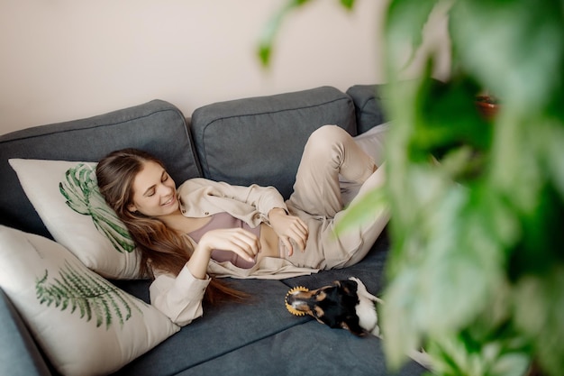 Young woman relaxing on sofa and playing with dog