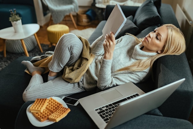 Young woman relaxing on the sofa and reading notes in the living room.