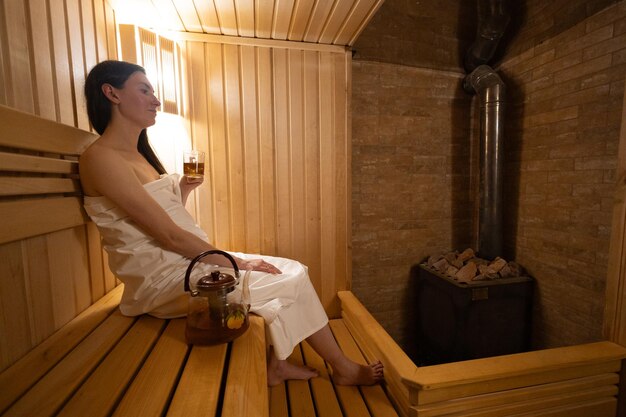 Young woman relaxing and sweating in hot sauna wrapped in towel girl in sauna interior of finnish sauna