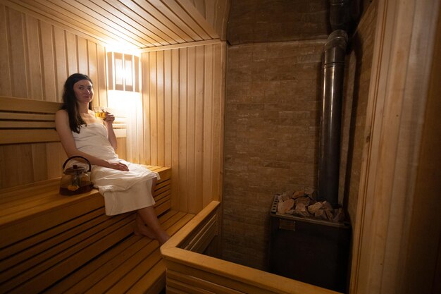 Young woman relaxing and sweating in hot sauna wrapped in towel Girl In Sauna Interior of Finnish sauna