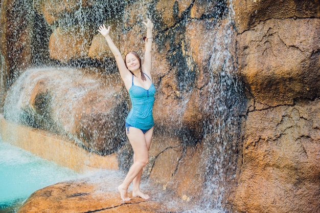 Young woman relaxing under a waterfall in aquapark