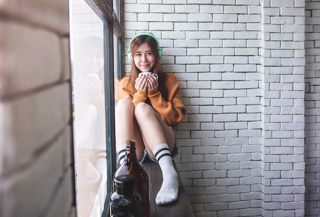 Young Woman Relaxing with Music From Headphone in Cozy House Nearby Window