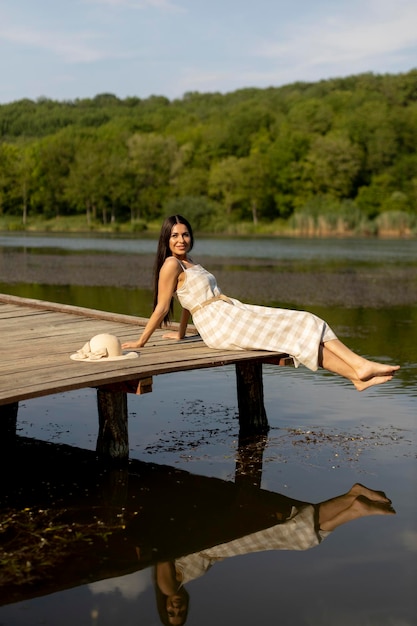 Young woman relaxing on the wooden pier at the calm lake