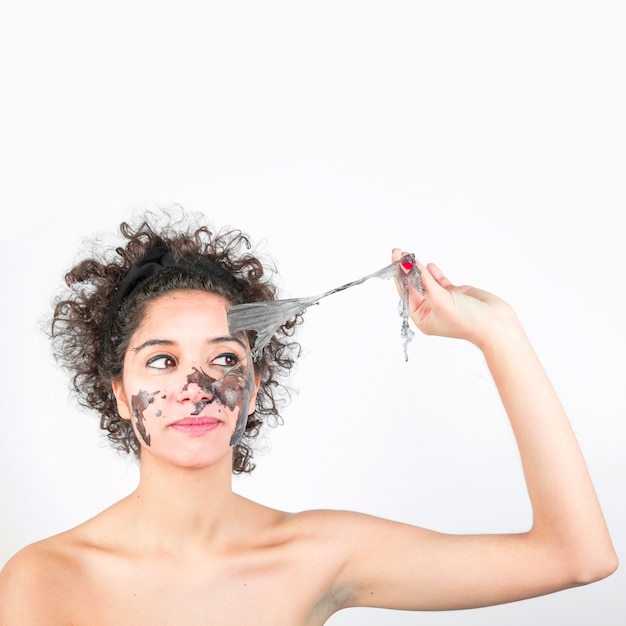 Young woman removing black mask on her face against white background