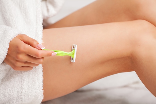 Foto giovane donna che rimuove i capelli sulle gambe con il rasoio in bagno.