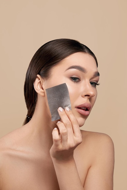 Young woman removing oil from face using blotting papers Skin care