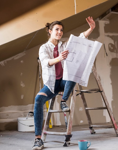 Foto giovane donna che rinnova la sua nuova casa, tenendo il piano di costruzione