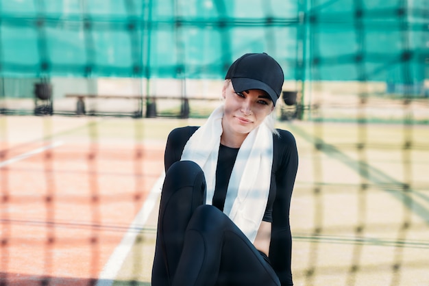 Young woman resting after doing sports on tennis court. Fitness and healthy lifestyle concept