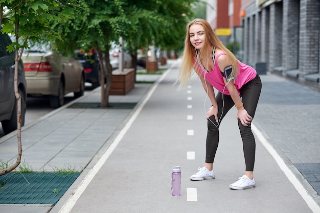 Young woman resting after running on a city lane with a bottle of water