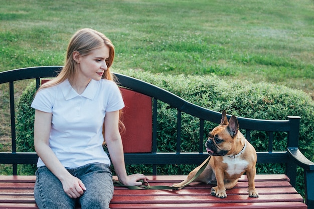 Young woman resting on a bench in the park with her dog in summer