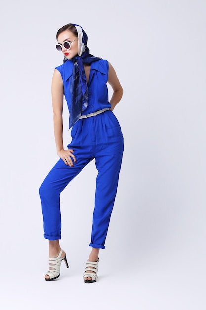 Young woman in retro style with sunglasses and silk scarf and blue overalls. Sixties style fashion retro woman.