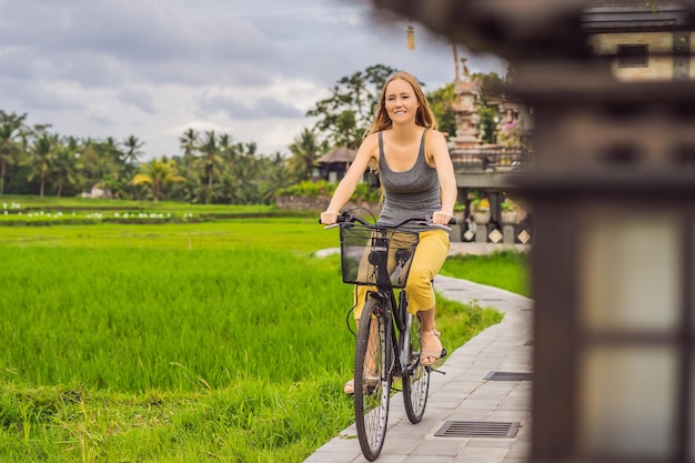 Молодая женщина едет на велосипеде по рисовому полю в Убуде Bali Bali Travel Concept