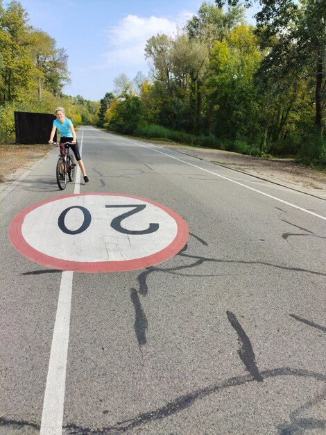 젊은 여성 이 공원 의 도로 에서 자전거 를 타고 있다. 속도 제한 표지판 이 그려져 있다.