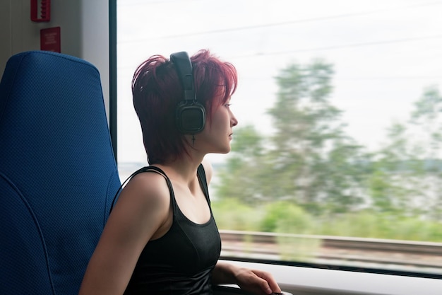 Young woman rides on a commuter train and looks out the window at an outside landscape blurred in motion