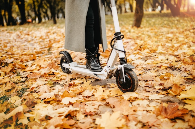 young woman riding an electric scooter in a city park in autumn
