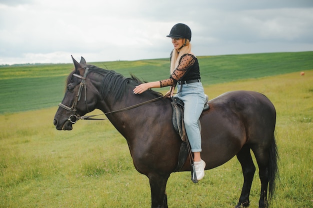 Young woman riding a horse on the green field