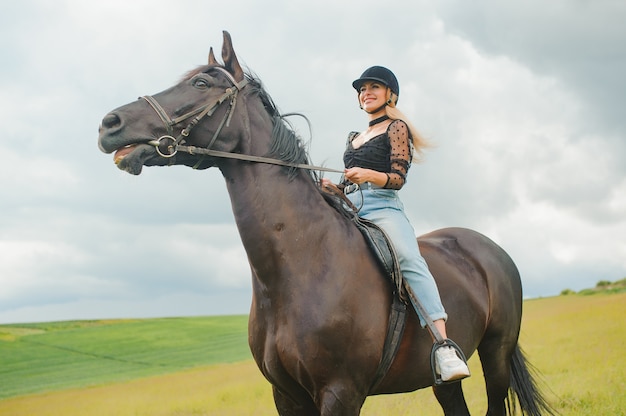 Young woman riding a horse on the green field