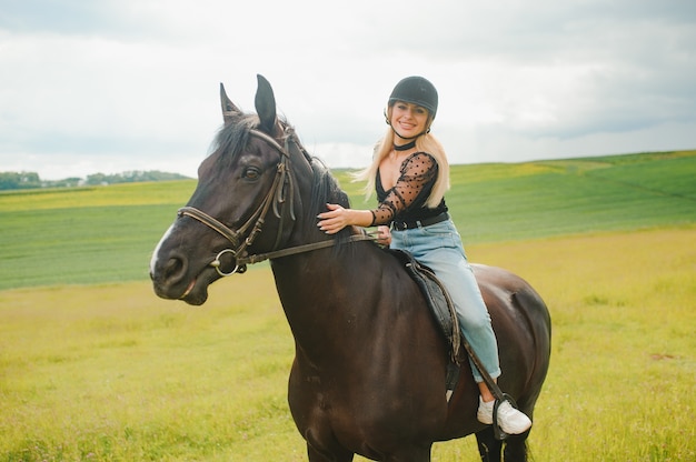 Young woman riding a horse on the green field