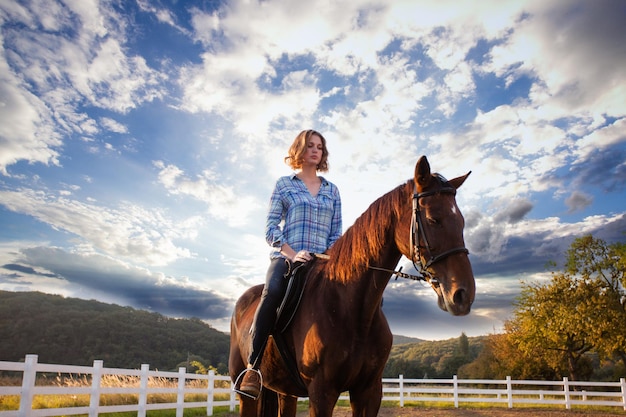 A young woman riding a horse looks at the sunset