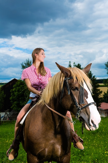 牧草地で馬に乗る若い女性