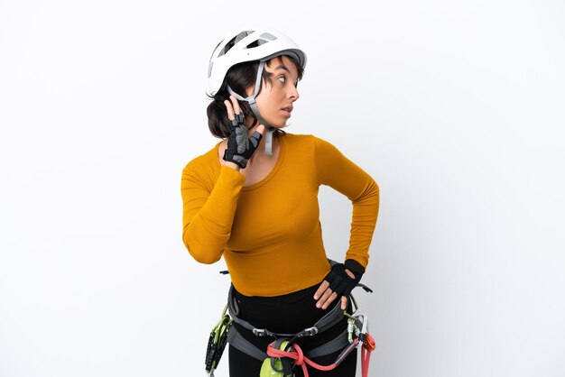 Young woman rock-climber woman isolated on white background listening to something by putting hand on the ear