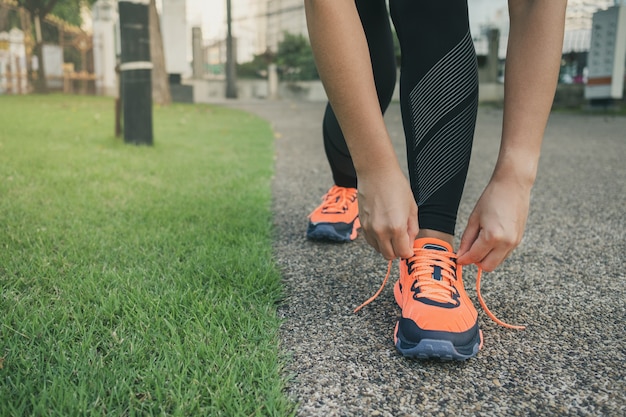 Corridore della giovane donna che lega le scarpe da corsa nel parco all'aperto