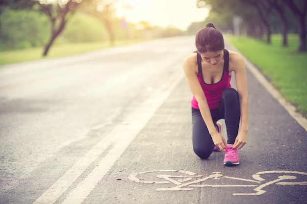 young woman runner tying shoelace on country road