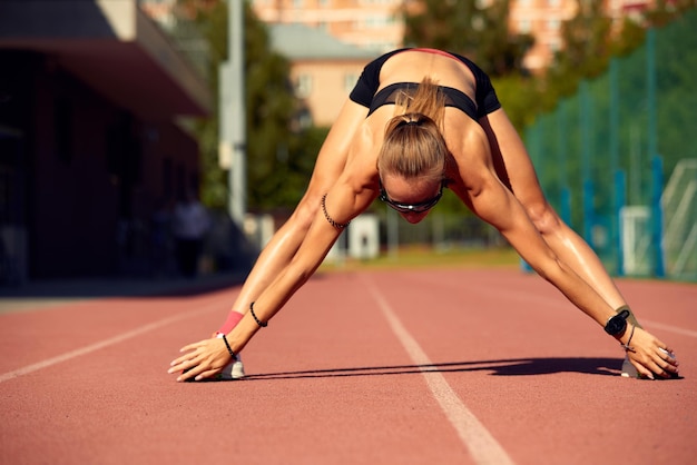 Corridore della giovane donna che si riscalda alla pista l'allenamento del corridore in forma allunga il suo muscolo e si riscalda alla pista