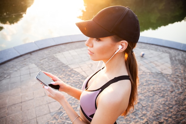 写真 腕章を身に着け、イヤホンで音楽を聴いている若い女性ランナー。アウトドアトレーニングから休憩するフィットスポーツウーマン