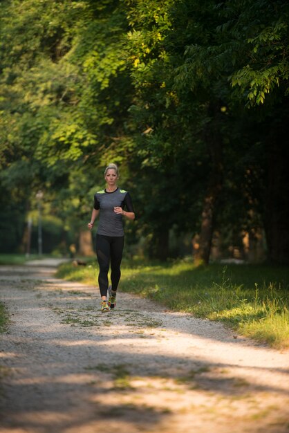 樹木が茂った森のエリアで走っている若い女性-トレイルランマラソンの耐久性のためのトレーニングと運動-フィットネス健康的なライフスタイルのコンセプト