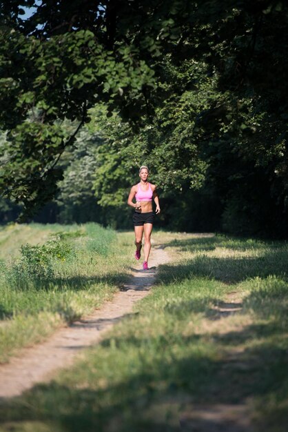 樹木が茂った森のエリアで走っている若い女性-トレイルランマラソンの耐久性のためのトレーニングと運動-フィットネス健康的なライフスタイルのコンセプト