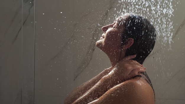 Young woman runs hands on face standing under shower water