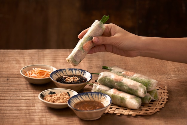 Young woman's hands eating healthy spring roll dipped in a soya sauce