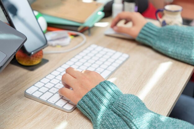 Le mani della giovane donna che digitano sulla tastiera del computer desktop mentre si lavora a casa