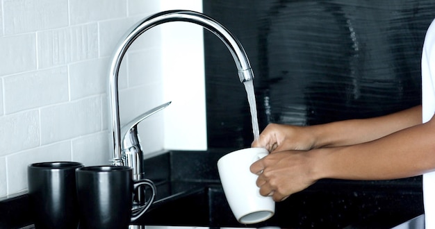 Foto le mani della giovane donna che lavano una tazza bianca con acqua.