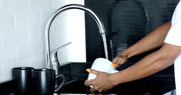 Young woman's hands washing a white cup with water.