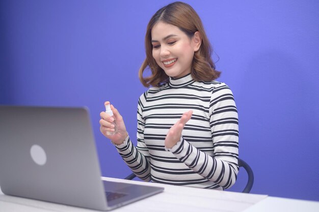 Young woman sanitizing alcohol spray with computer , covid-19 protection concept .