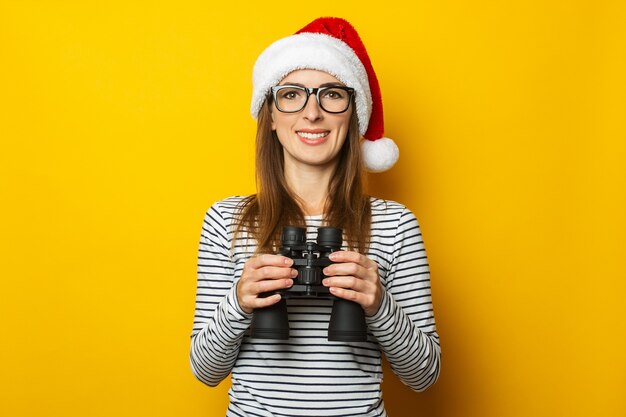 Young woman in a Santa Claus hat holds binoculars