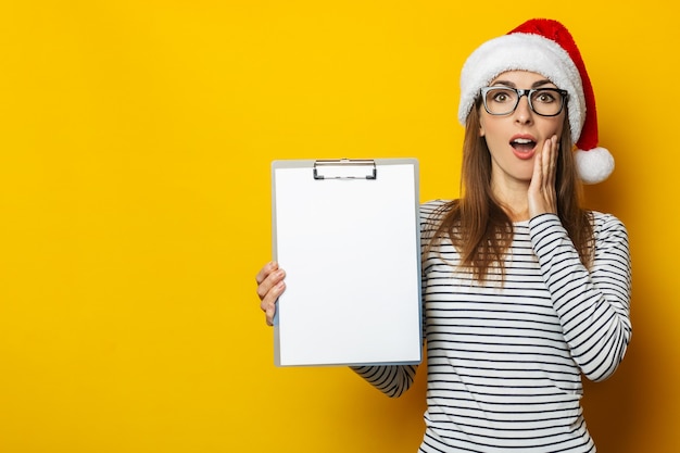 Young woman in a santa claus hat holds an empty clipboard