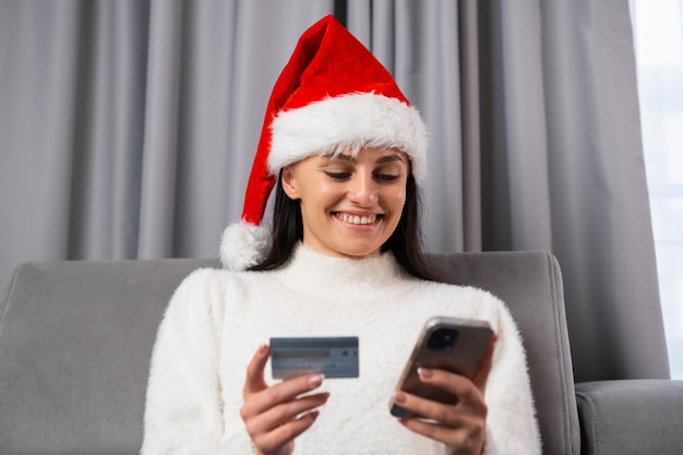 A young woman in Santa Claus hat orders gifts online Spending money at home